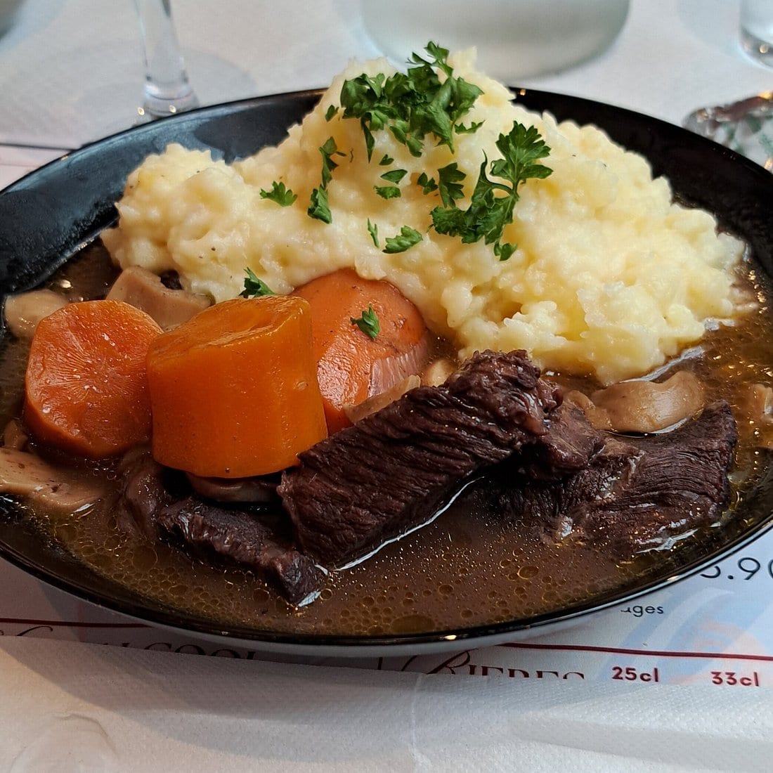 Une assiette de viande en sauce, carottes et purée parsemée de persil