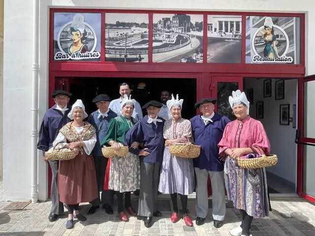 Un groupe en costumes traditionnels et coiffes sablaises devant le restaurant